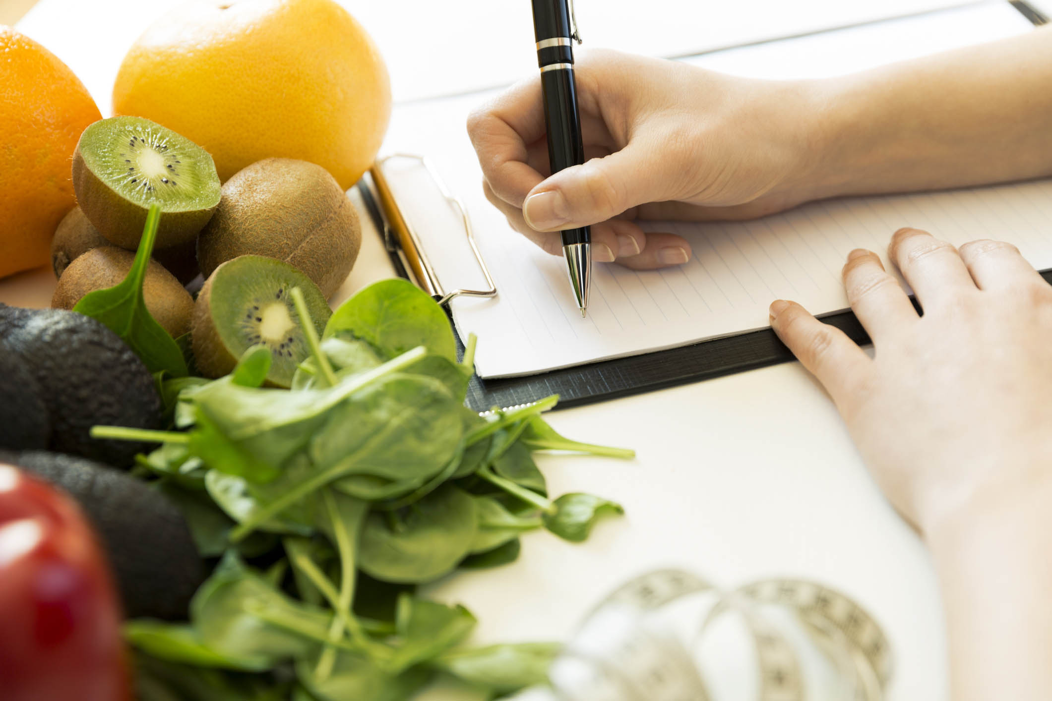 Nutritionist woman writing diet plan on table full of fruits and vegetables